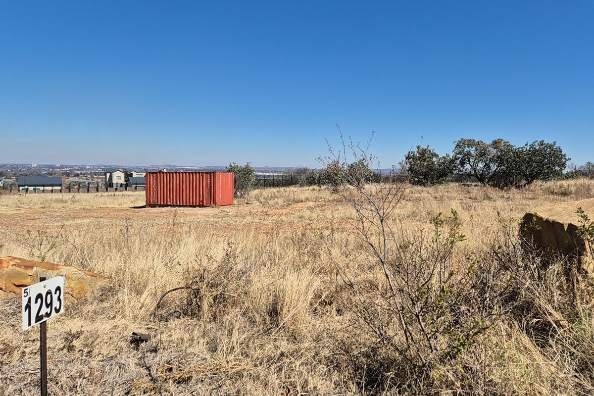 A view of a vacant residential plot featuring dry grass, natural vegetation, and a boundary marker post.