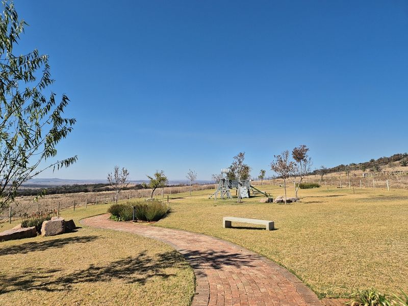 A well-maintained garden area featuring a winding brick paved pathway, a stone bench, and expansive lawn space with scenic landscape views.
