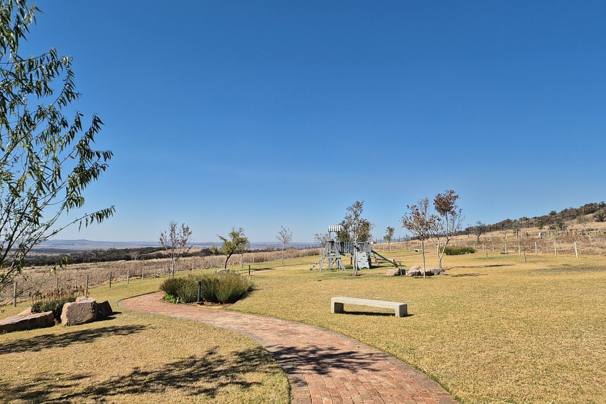 A well-maintained garden area featuring a winding brick paved pathway, a stone bench, and expansive lawn space with scenic landscape views.