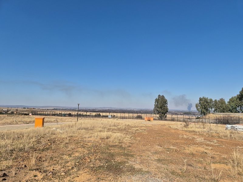 An expansive view of the surrounding landscape from the vacant residential plot, featuring perimeter fencing and clear horizon lines.
