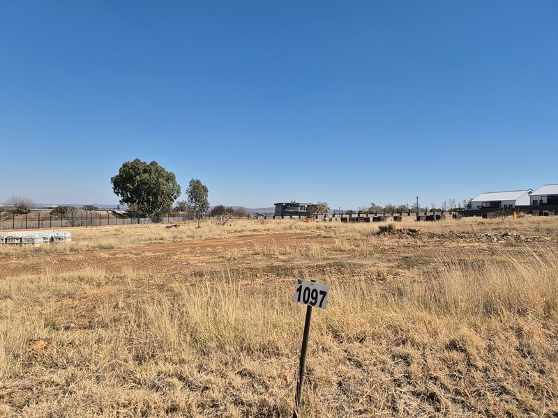 A vacant residential plot of land featuring natural grass coverage and perimeter fencing, ready for development in a residential estate.