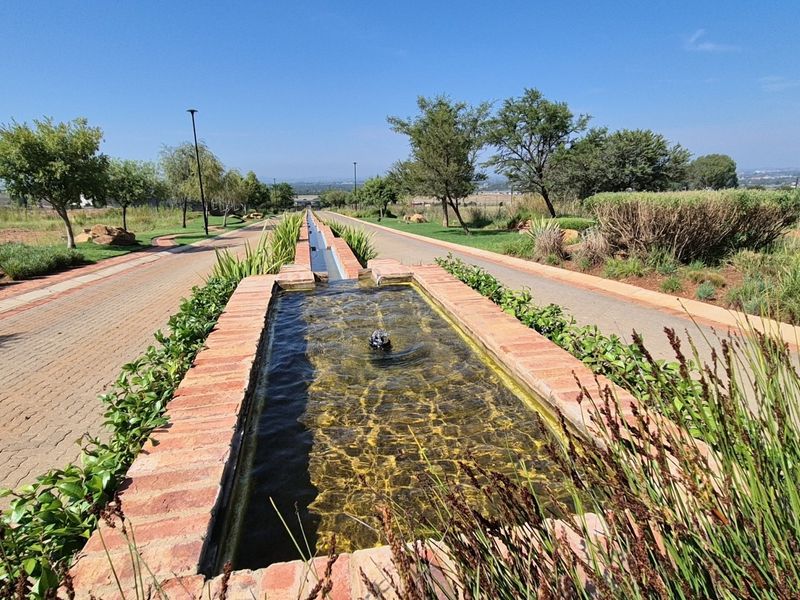 A well-maintained landscaped garden featuring a long brick water feature and paved walkways leading through the residential estate.