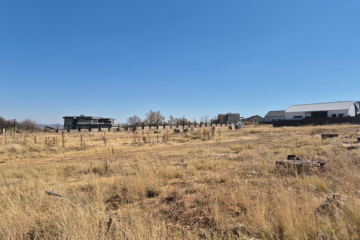 A view of a vacant residential plot featuring dry grass and perimeter fencing, situated in a developing neighborhood.