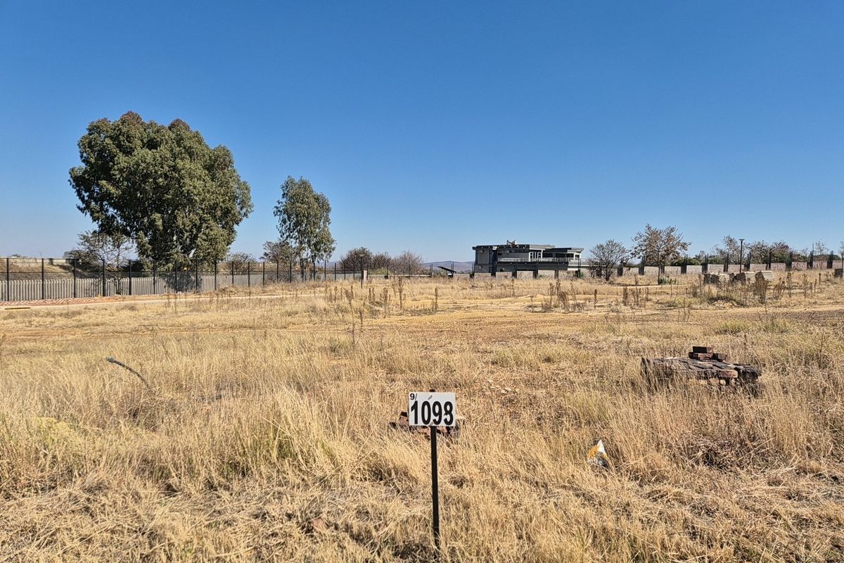 A vacant residential plot featuring dry grass, perimeter fencing, and a clear lot marker, ready for development.