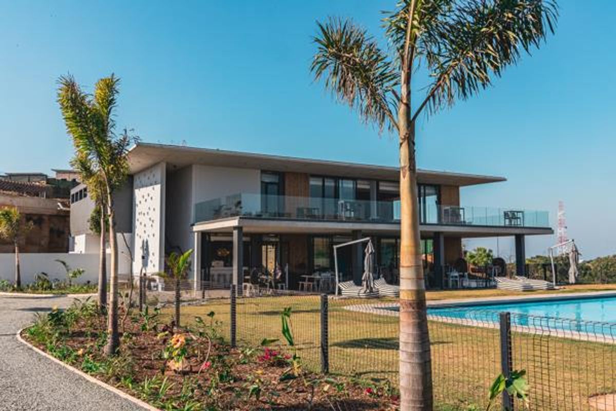 A modern two-story residential property featuring a spacious rear patio, glass balcony railings, and a well-maintained swimming pool set within a landscaped garden.
