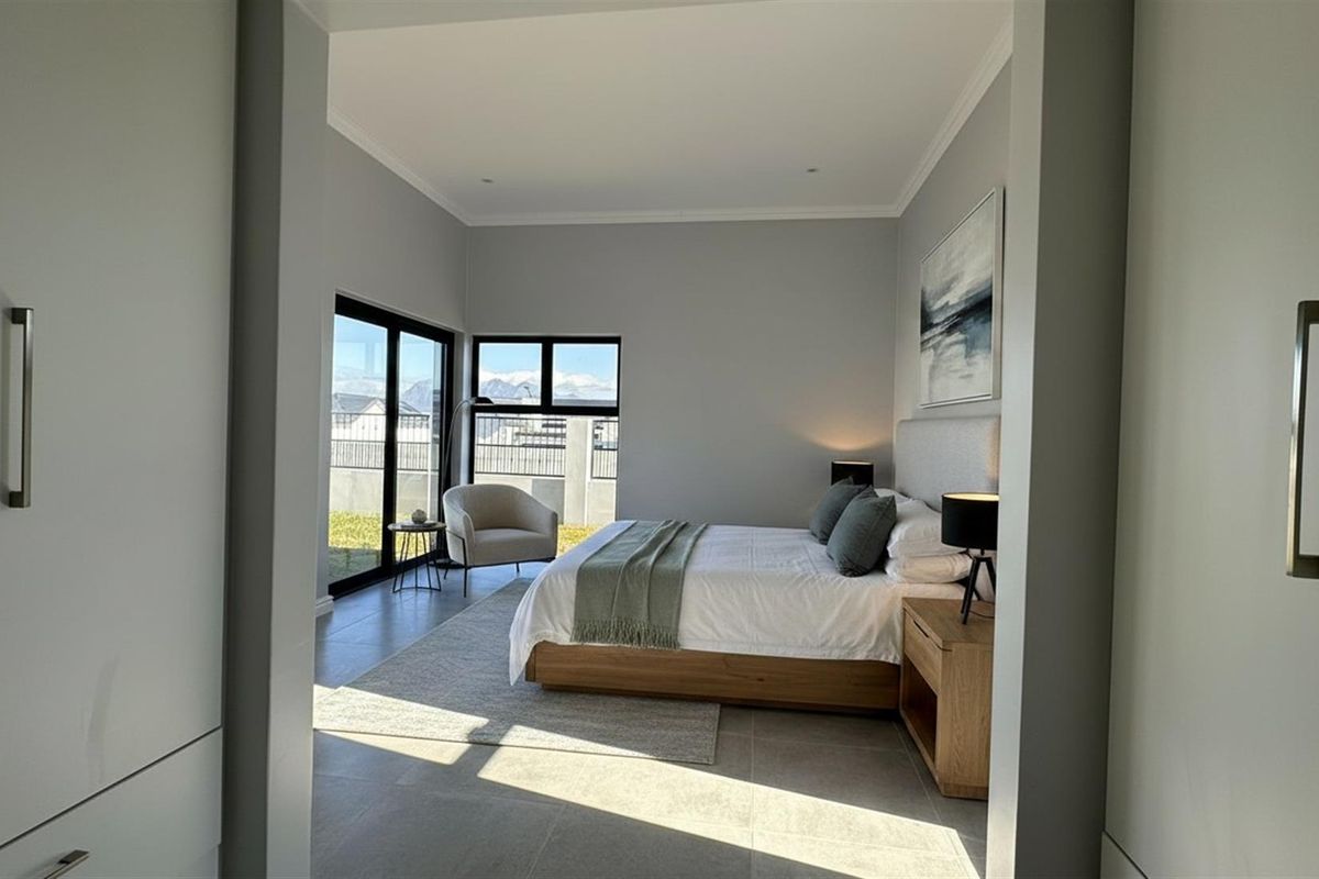 A modern, well-lit bedroom featuring large sliding glass doors, neutral tiled flooring, and built-in cabinetry, offering a clean and contemporary living space.