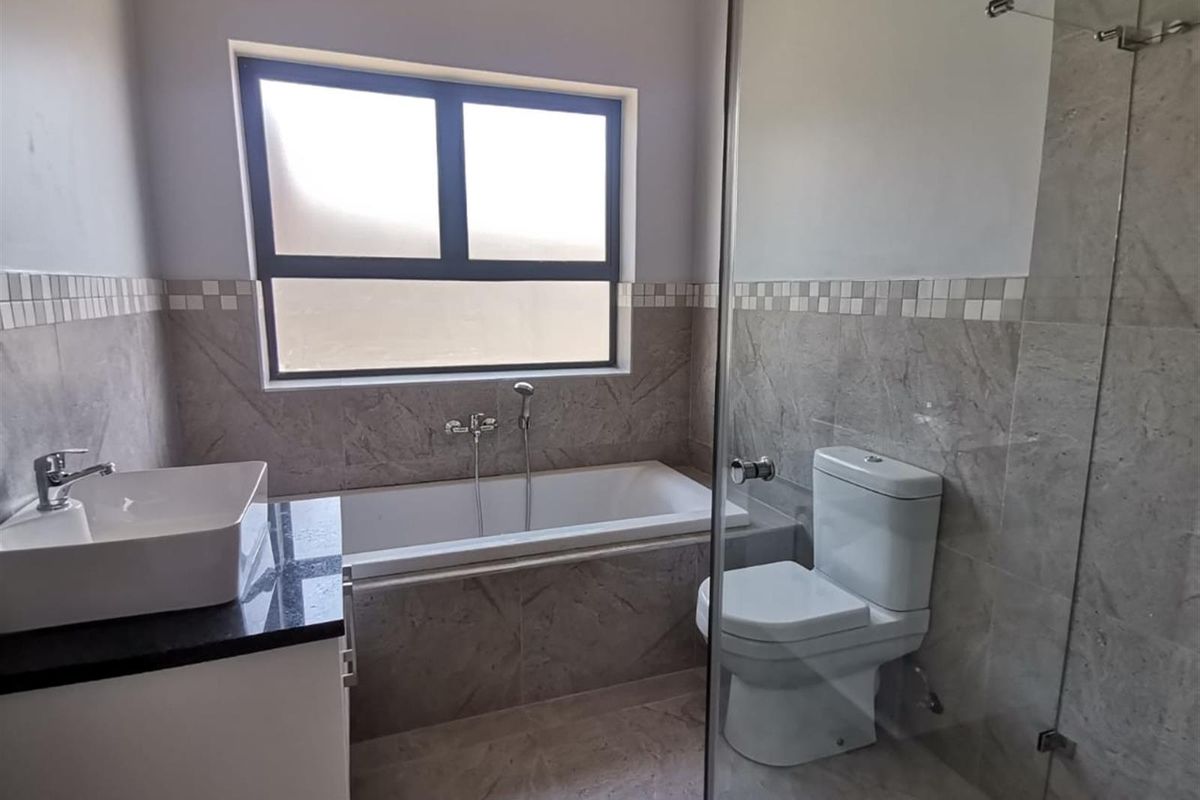 Modern bathroom featuring a built-in bathtub, glass-enclosed shower, vanity with basin, and neutral wall tiling.