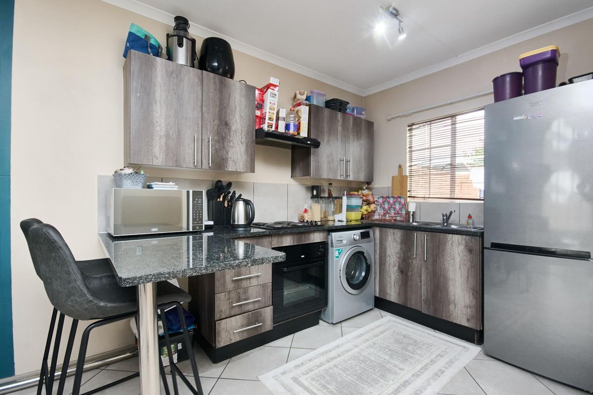 Compact kitchen featuring wood-look cabinetry, granite countertops, built-in oven, hob, extractor fan, and integrated space for a washing machine.