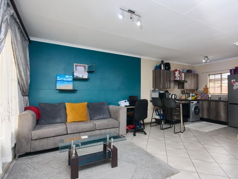 An open-plan living area featuring a kitchen with dark cabinetry, tiled flooring, and a dedicated lounge space with a feature wall.