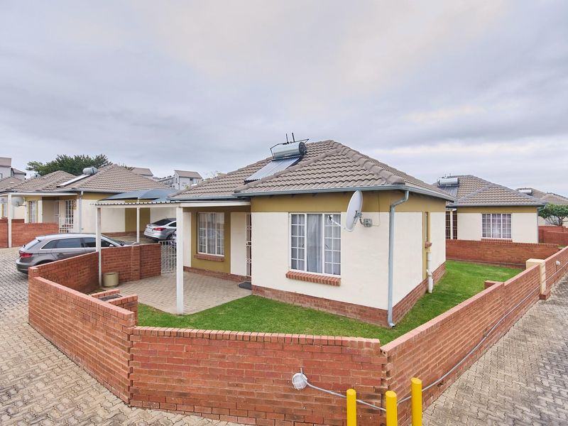 A detached single-story residential house featuring a tiled roof, solar water heating system, paved patio area, and a surrounding brick boundary wall.