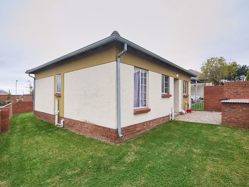 Rear view of the house featuring a paved patio area, brick boundary walls, and a well-maintained lawn.