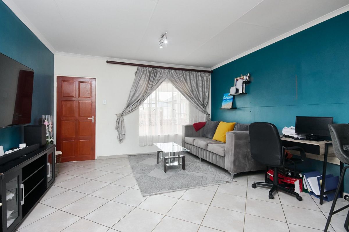 A functional living room featuring tiled flooring, a bold teal accent wall, and a solid timber door, providing a versatile space for relaxation.