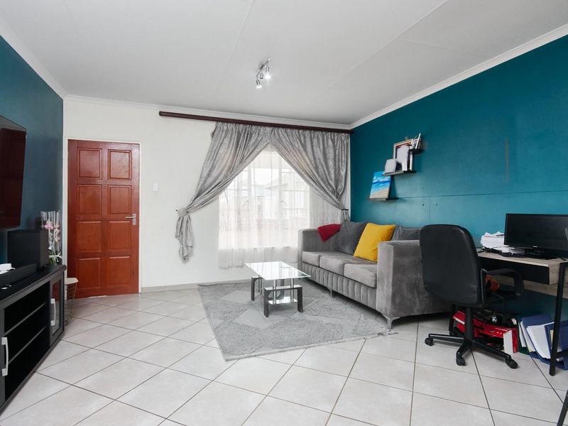 A functional living room featuring tiled flooring, a bold teal accent wall, and a solid timber door, providing a versatile space for relaxation.