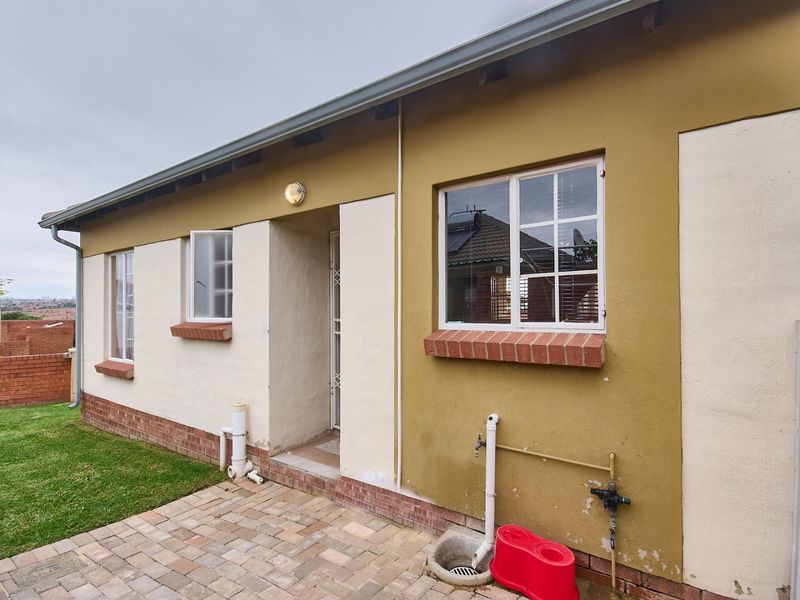 A view of the rear exterior of the house featuring a paved patio area, brick accents, and access to the garden.