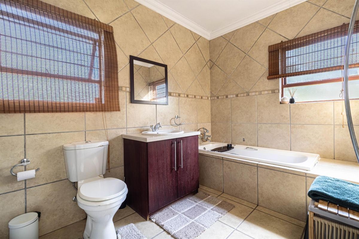 A functional bathroom featuring full-height wall tiling, a built-in bathtub, a vanity cabinet with a basin, and a toilet.