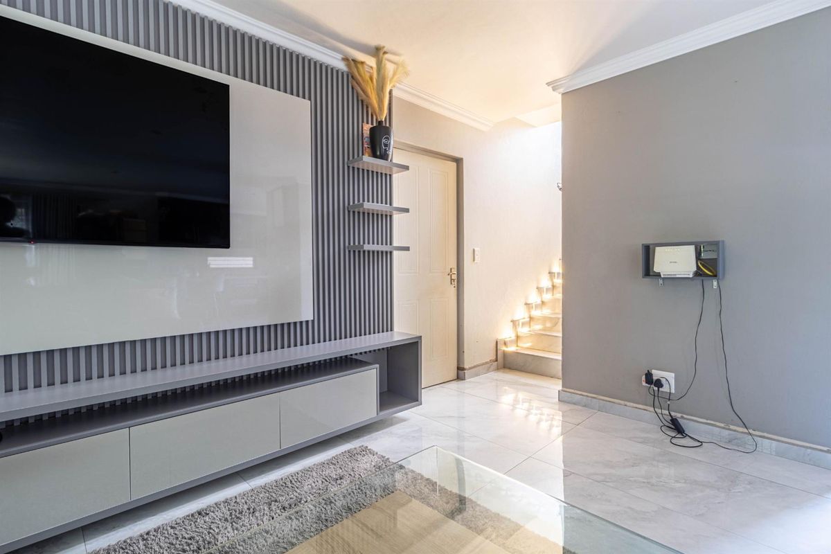 Modern living room featuring a sleek built-in media console, decorative slat wall paneling, polished tile flooring, and integrated staircase lighting.