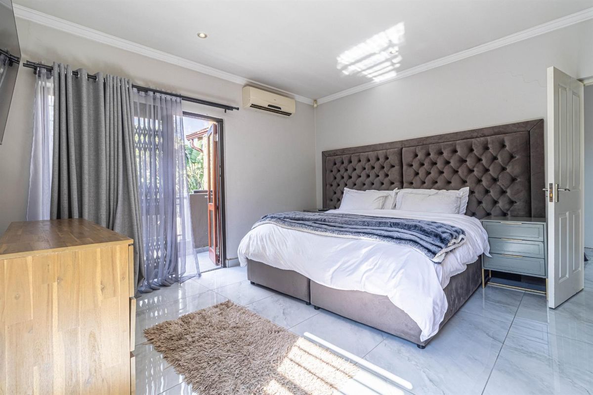 Spacious bedroom featuring polished tile flooring, recessed ceiling lighting, a wall-mounted air conditioning unit, and direct access to a private balcony.