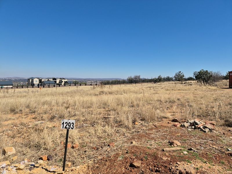 A vacant residential plot featuring dry grass, a boundary fence, and a clear view of the surrounding neighborhood.