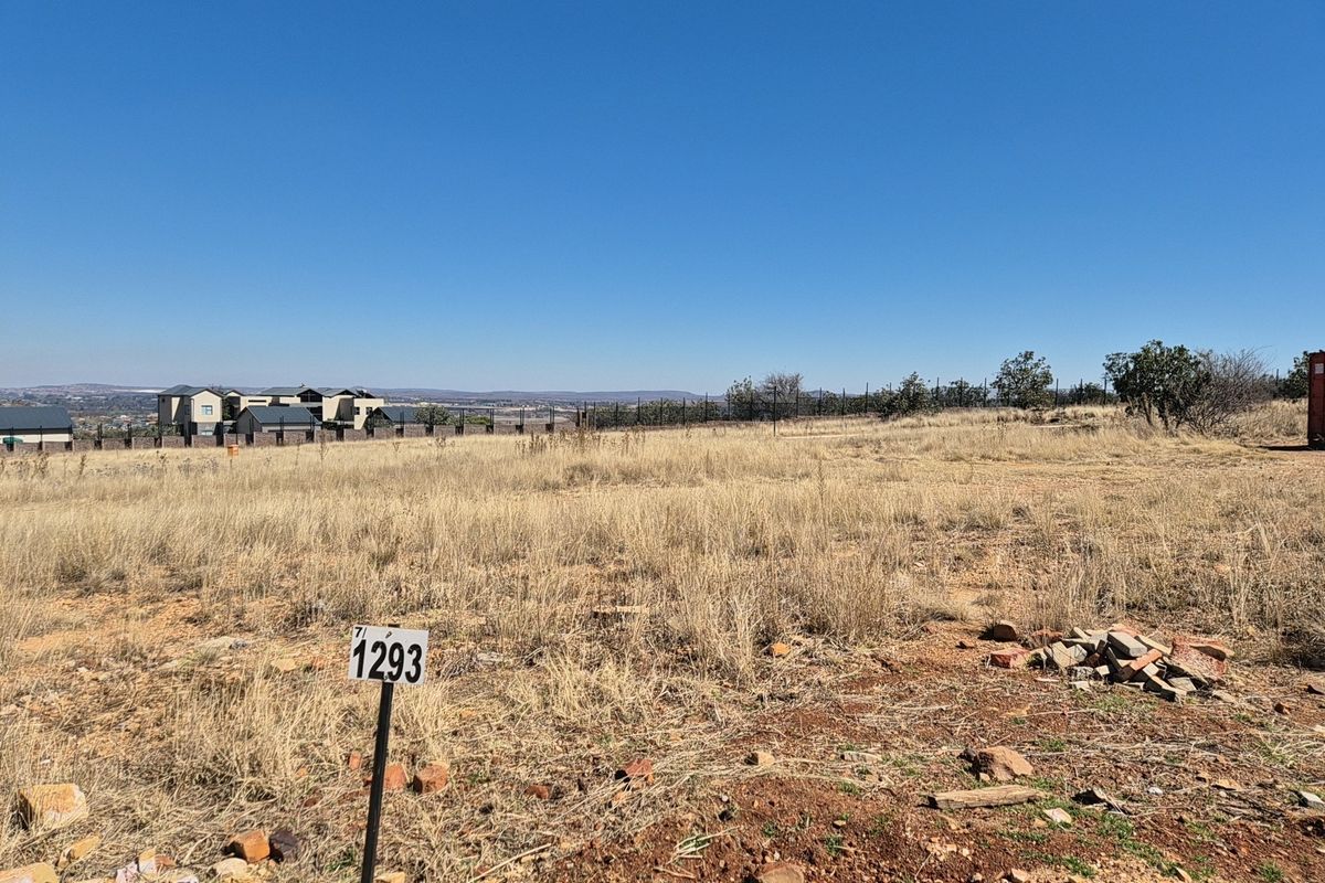 A vacant residential plot featuring dry grass, a boundary fence, and a clear view of the surrounding neighborhood.