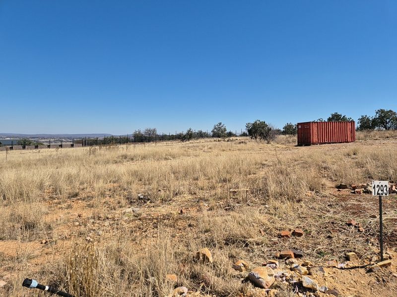 A vacant residential plot featuring dry grass, perimeter fencing, and a clear view of the surrounding landscape.