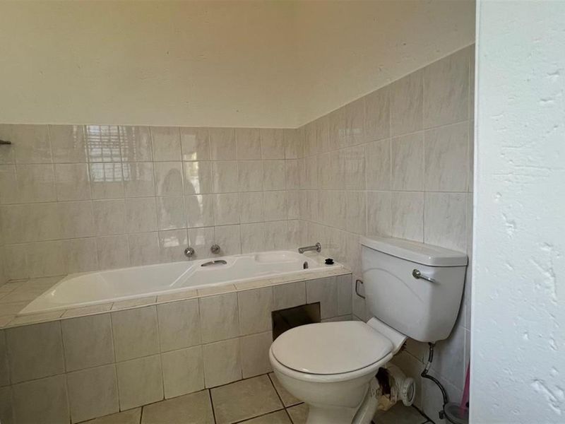 A functional bathroom featuring a built-in bathtub and standard toilet, finished with ceramic wall and floor tiles.