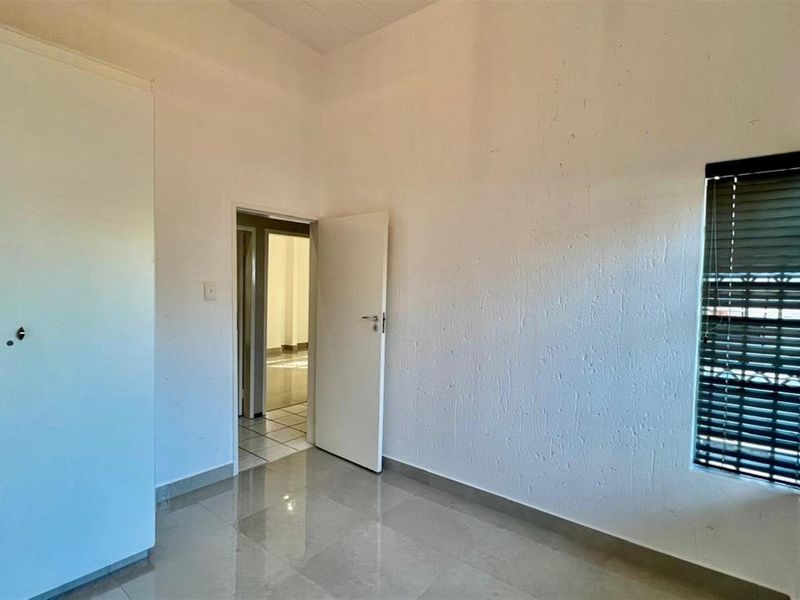 An empty bedroom featuring tiled flooring, a built-in wardrobe, and venetian blinds on the window.