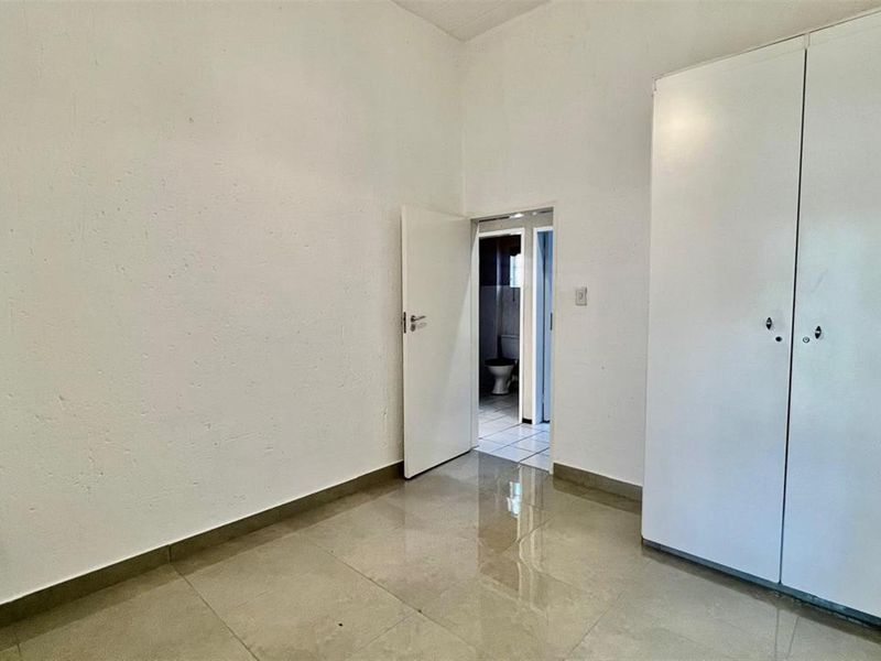 A clean, empty bedroom featuring tiled flooring, a built-in wardrobe, and direct access to an en-suite bathroom.