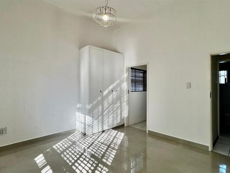 A bright, empty bedroom featuring neutral tiled flooring, a built-in wardrobe, and clean white walls, offering a versatile space ready for personalization.