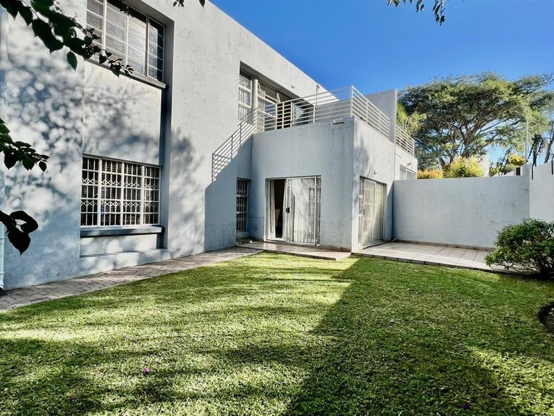 Rear view of the townhouse featuring a private garden, paved patio area, and an upper-level balcony with security features.