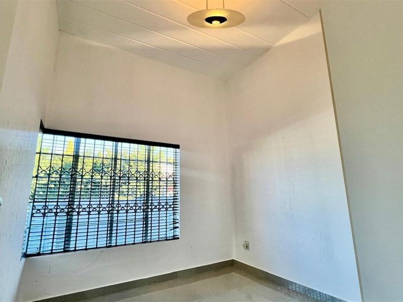 An empty bedroom featuring tiled flooring, a ceiling light fixture, and a window fitted with security bars.