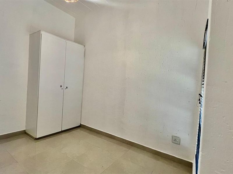 A clean, empty bedroom featuring neutral tiled flooring, white walls, and a built-in wardrobe, offering a blank canvas for personalization.