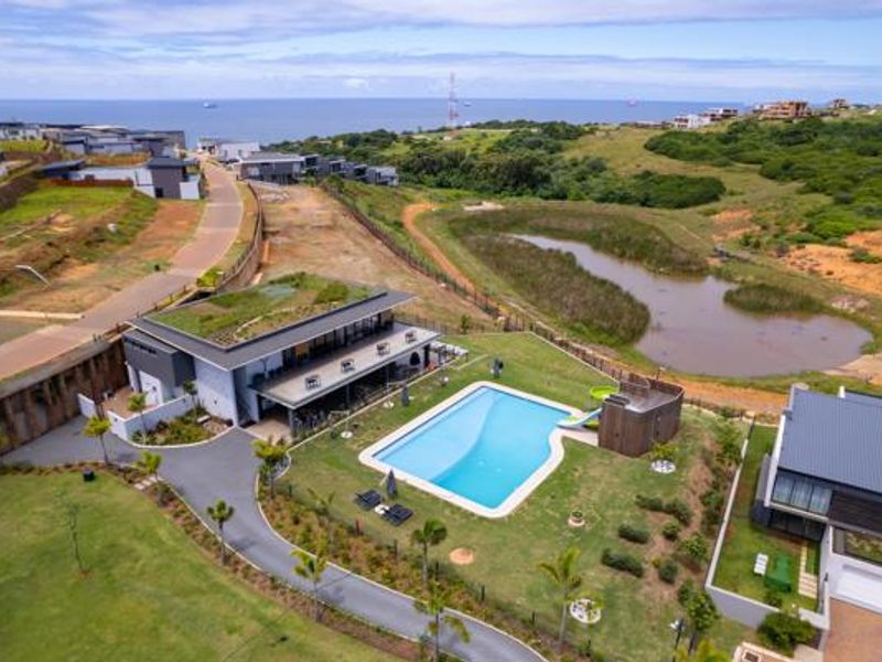 Aerial view of a modern residential property featuring a swimming pool, landscaped garden, and green roof, situated in a coastal estate setting.