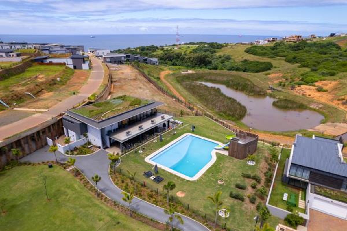 Aerial view of a modern residential property featuring a swimming pool, landscaped garden, and green roof, situated in a coastal estate setting.