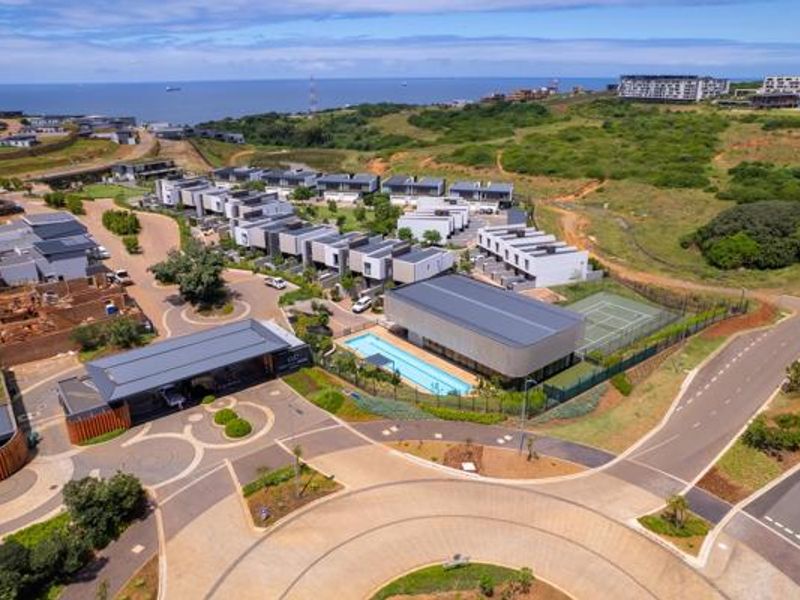Aerial view of a modern residential estate featuring a clubhouse, swimming pool, tennis court, and surrounding landscaped grounds with coastal views.
