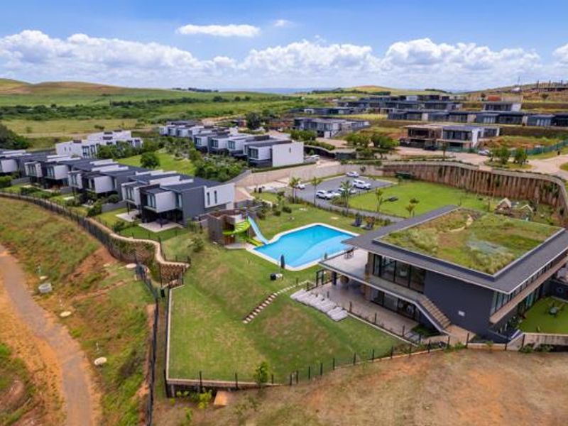 Aerial view of a modern residential estate featuring contemporary homes, a central swimming pool, landscaped gardens, and green roof architecture.