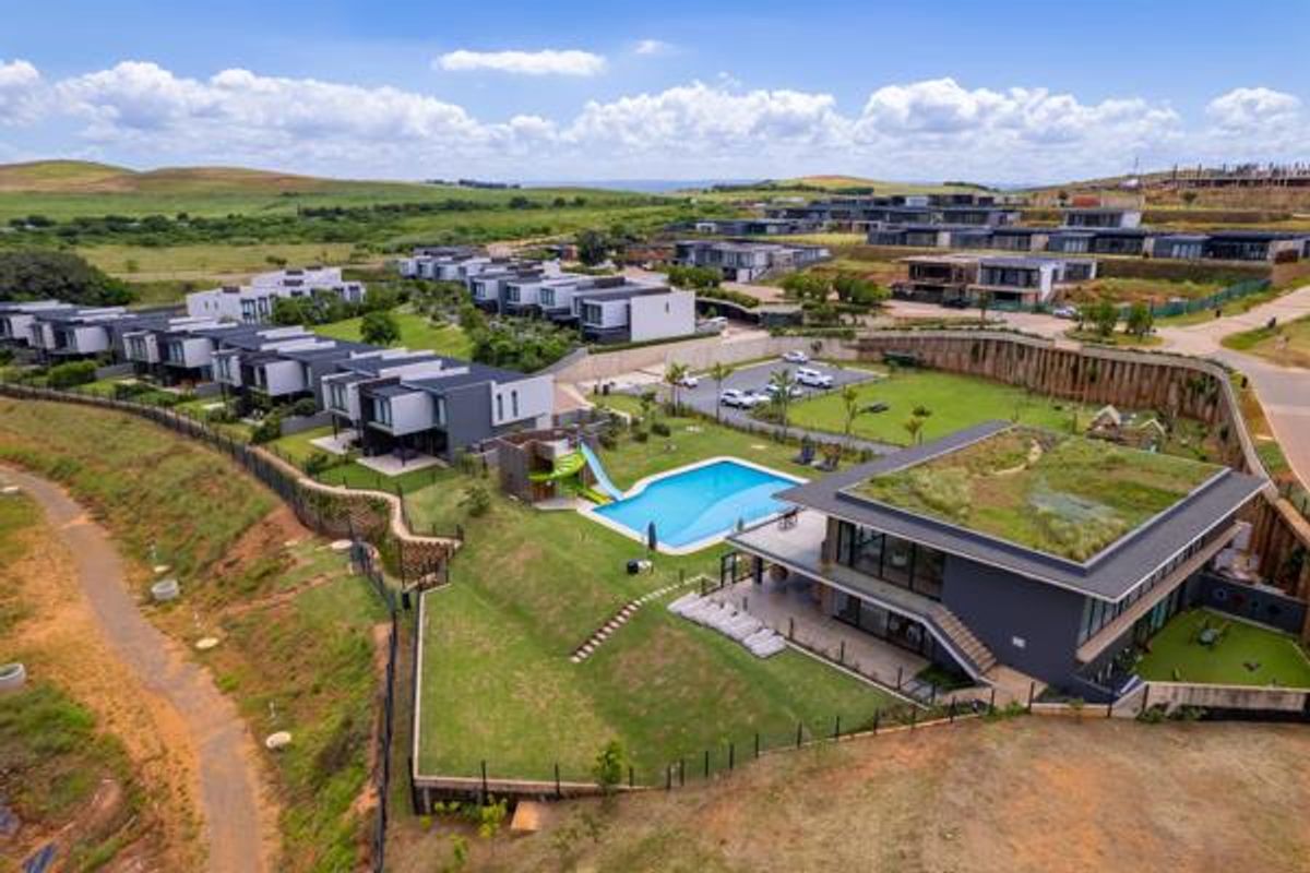 Aerial view of a modern residential estate featuring contemporary homes, a central swimming pool, landscaped gardens, and green roof architecture.