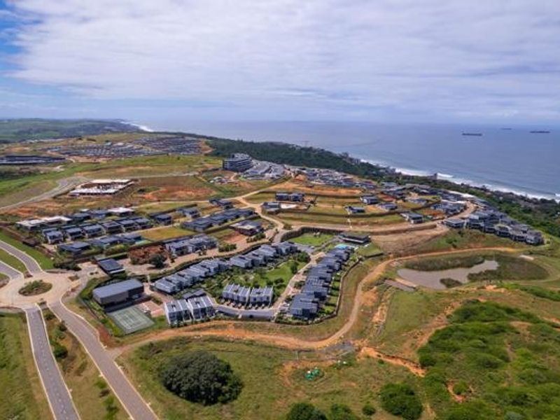 Aerial view of a coastal residential estate development featuring modern housing clusters, paved road infrastructure, and proximity to the ocean.