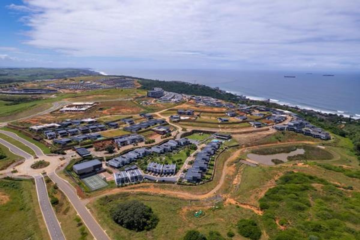 Aerial view of a coastal residential estate development featuring modern housing clusters, paved road infrastructure, and proximity to the ocean.