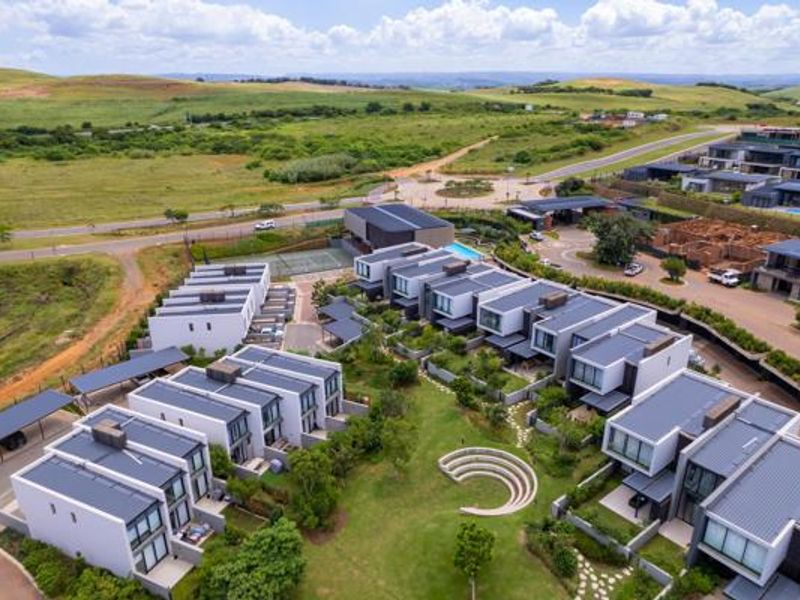 Aerial view of a modern residential estate featuring contemporary townhouses, landscaped green spaces, a central amphitheater, and communal recreational facilities.