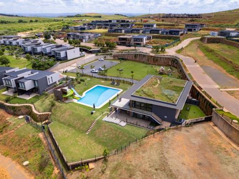 Aerial view of a modern residential estate featuring a swimming pool, landscaped gardens, and contemporary homes with green roof architecture.