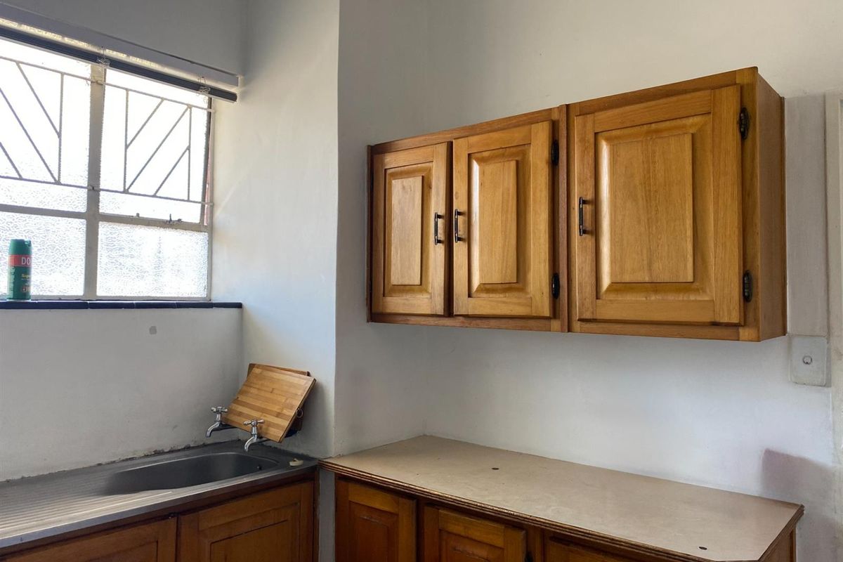 A functional kitchen area featuring traditional wooden cabinetry, a stainless steel sink, and a window with security bars, offering a blank canvas for renovation.