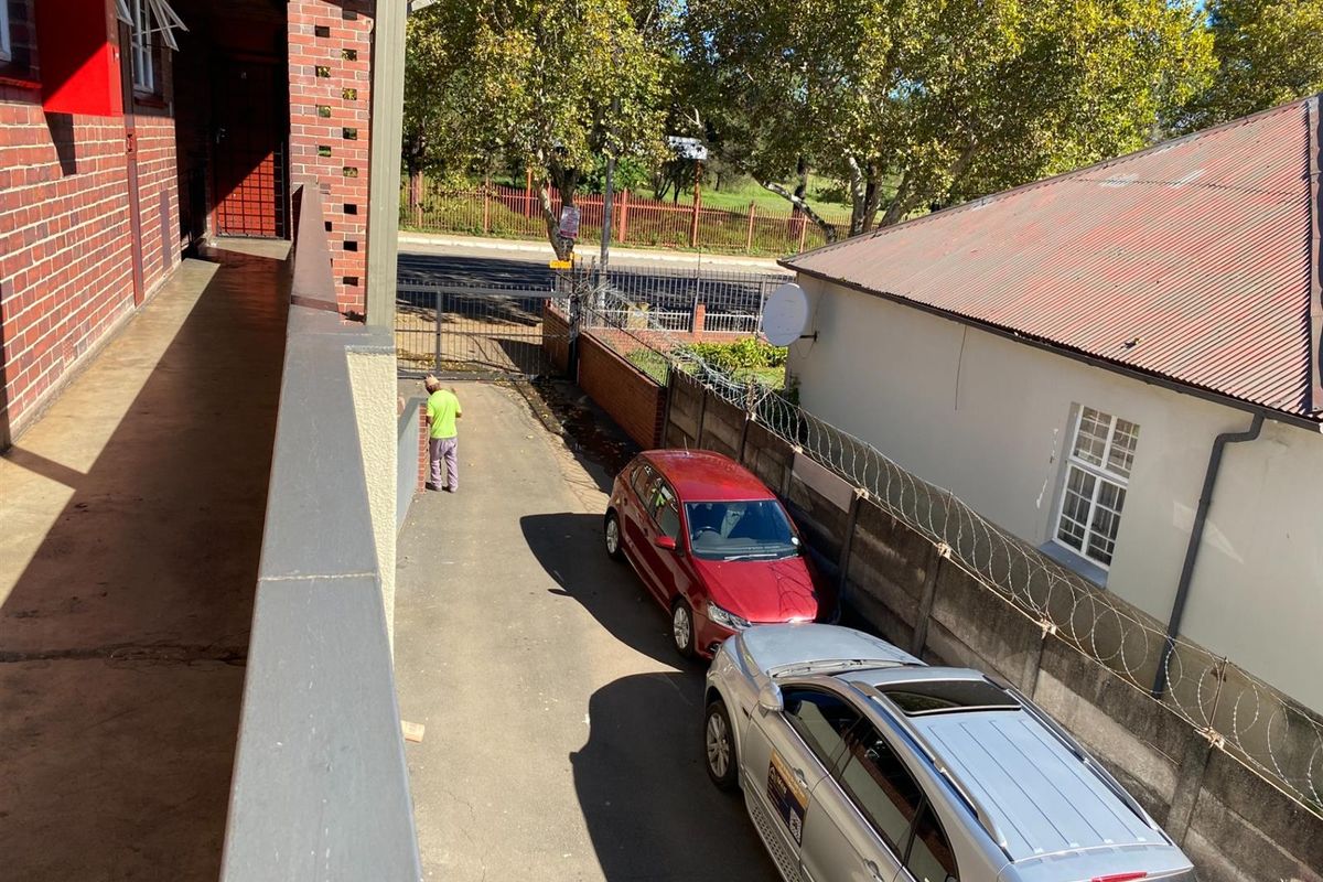 An elevated view of the rear exterior area showing a driveway, brick building facade, and perimeter security fencing.