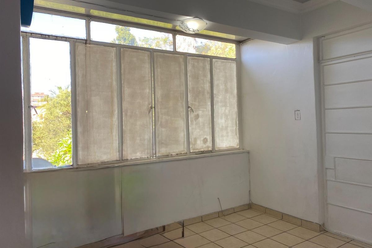 An empty living area featuring tiled flooring, large windows with screens, and neutral walls, offering a blank canvas for renovation and interior design.