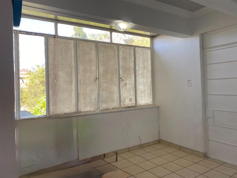 An empty living area featuring tiled flooring, large windows with screens, and neutral walls, offering a blank canvas for renovation and interior design.