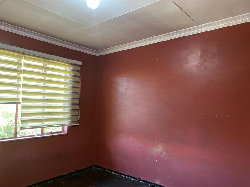 An empty bedroom featuring parquet flooring, crown molding, and roller blinds, currently requiring cosmetic updates to the wall paint and flooring.