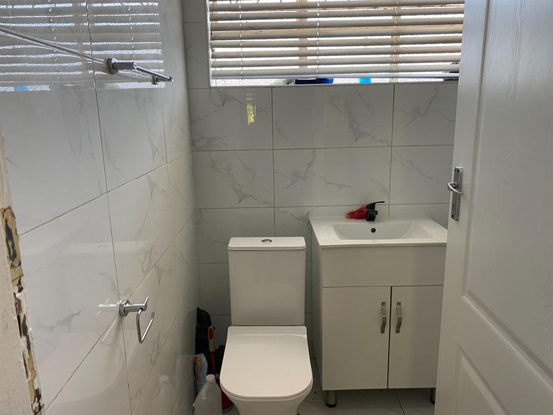 A compact bathroom featuring white marble-look wall tiles, a modern vanity unit with basin, and a standard toilet.