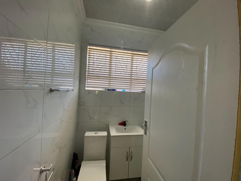 A compact, modern bathroom featuring white marble-look wall tiles, a vanity basin, and a toilet, finished with clean lines and functional fixtures.
