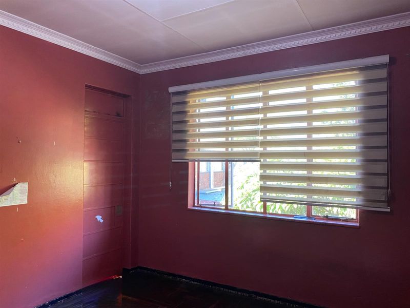 An empty bedroom featuring parquet flooring, crown molding, and zebra blinds. The room requires cosmetic updates to the wall finishes and door.