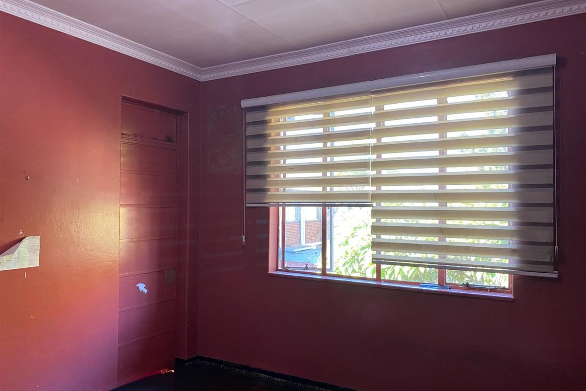 An empty bedroom featuring parquet flooring, crown molding, and zebra blinds. The room requires cosmetic updates to the wall finishes and door.