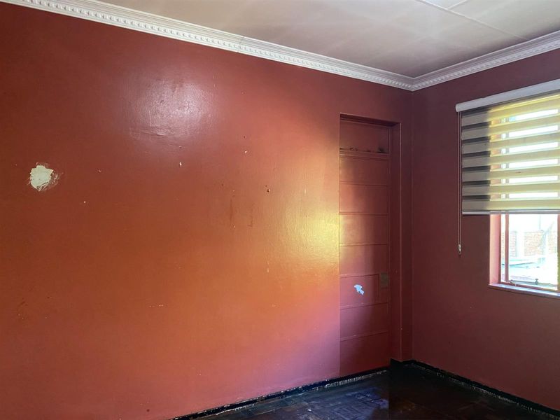 An empty bedroom featuring parquet flooring, crown molding, and a roller blind. The walls require cosmetic attention and repainting.